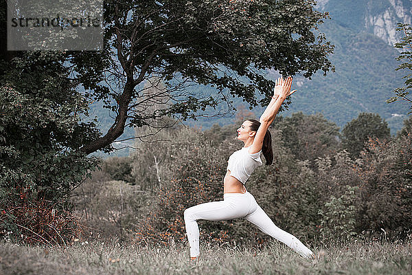 Yoga praktizierende Frau  Kriegerpose in ländlicher Landschaft