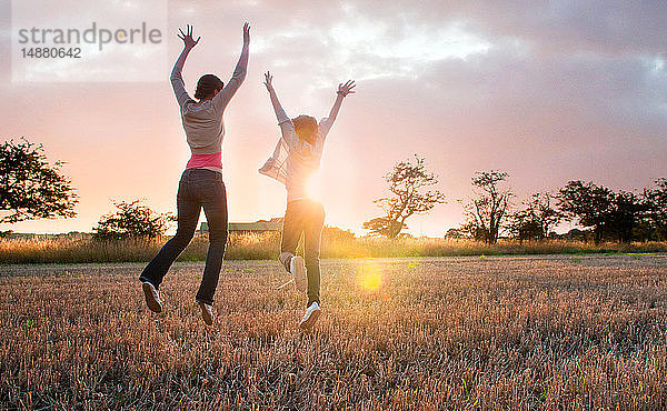 Zwei Mädchen springen vor Freude im sonnenbeschienenen Feld  Rückansicht
