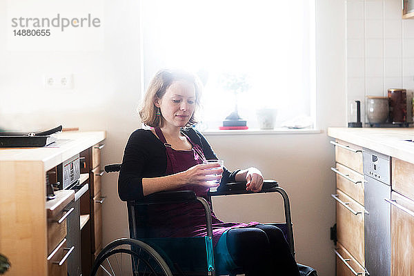 Frau im Rollstuhl mit einem Glas Wasser in der Küche