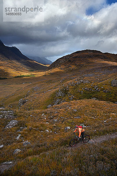 Männlicher Mountainbiker radelt auf Feldweg in Bergtal-Landschaft  erhöhte Ansicht  Achnasheen  Schottische Highlands  Schottland