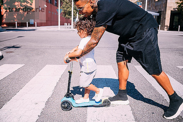 Vater lehrt Sohn Schiebemotorroller auf Fußgängerüberweg fahren
