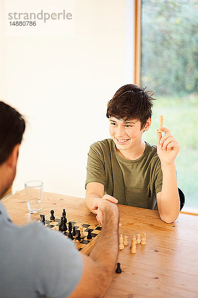 Junge und Vater schütteln sich die Hand beim Schachspiel am Wohnzimmertisch  Blick über die Schulter
