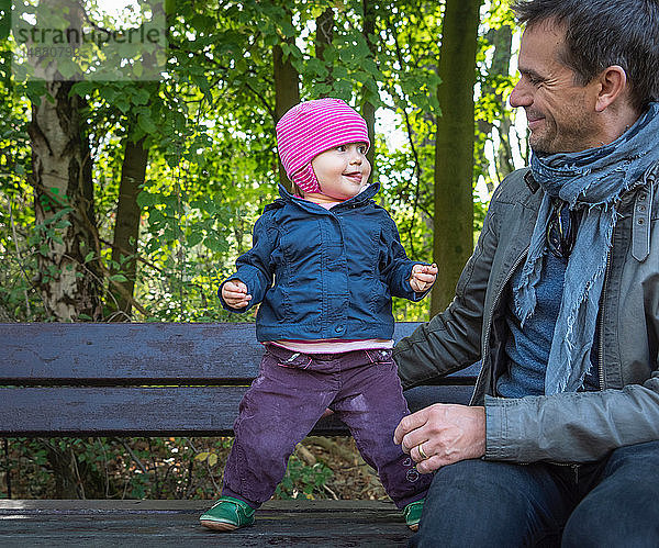 Vater und kleines Mädchen auf Parkbank am Wald