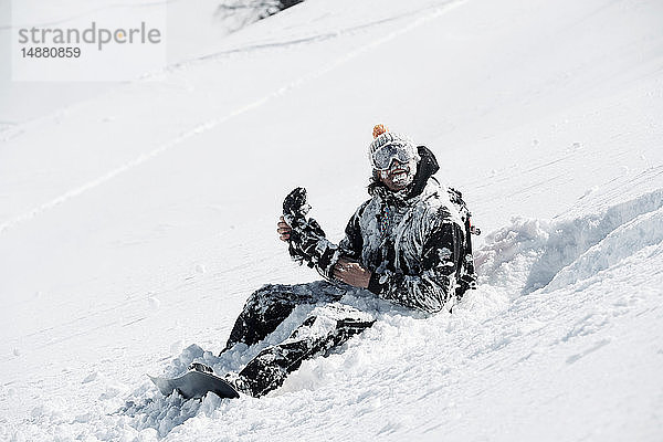 Schneebedeckter männlicher Snowboarder am Berghang sitzend  Alpe-d'Huez  Rhône-Alpes  Frankreich