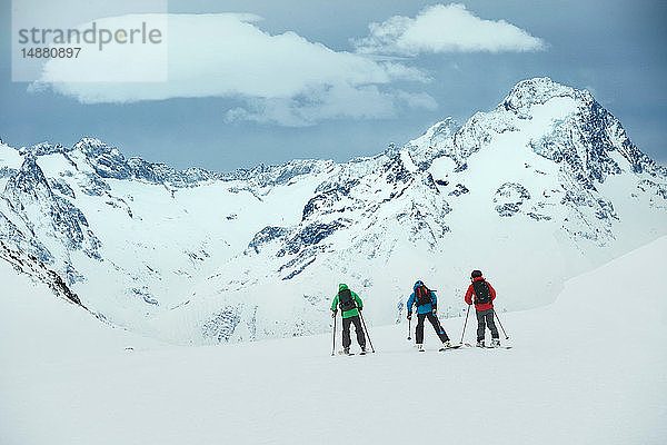 Landschaft mit drei männlichen Skifahrern  die in Richtung Berg fahren  Rückansicht  Alpe-d'Huez  Rhône-Alpes  Frankreich