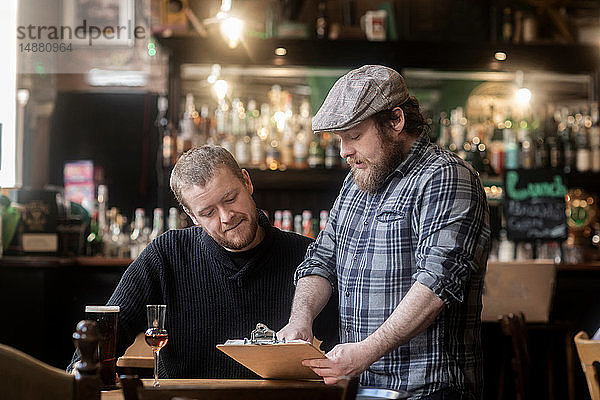 Barkeeper betrachtet Speisekarte mit einem Gast in einem traditionellen irischen Lokal