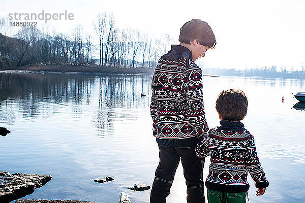Junge und kleiner Bruder in passenden Pullovern am Seeufer stehend  Comer See  Lecco  Lombardei  Italien