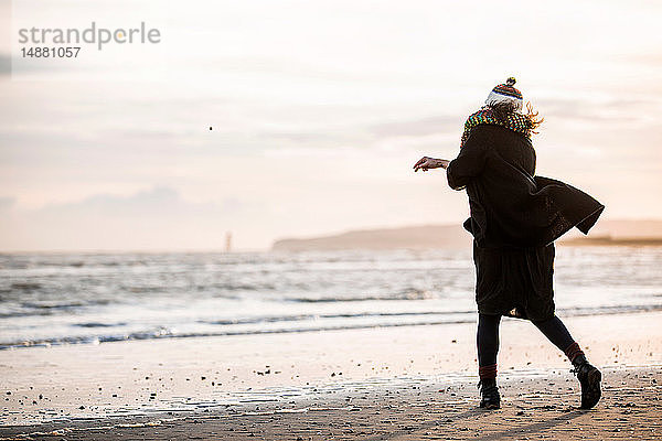 Frau wirft Kieselsteine an den Strand