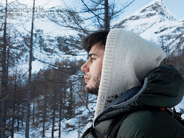 Mittelgroßer erwachsener Mann im Kapuzenpullover in schneebedeckter Bergwaldlandschaft  Porträt  Alpe Ciamporino  Piemont  Italien