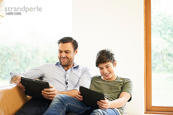 Junge und Vater schauen auf digitale Tabletts  während sie auf dem Sofa liegen