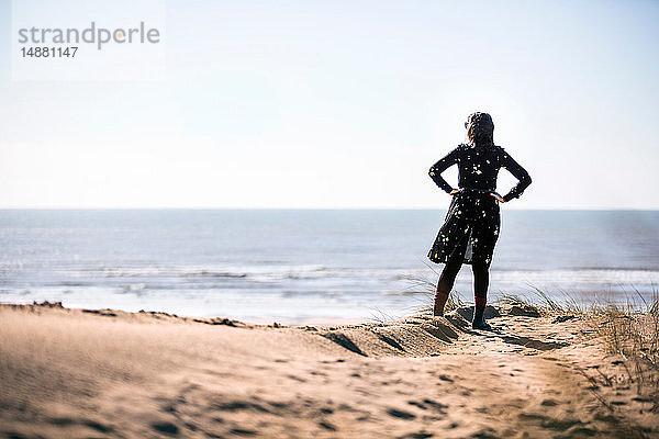 Frau schaut am Strand aufs Meer hinaus