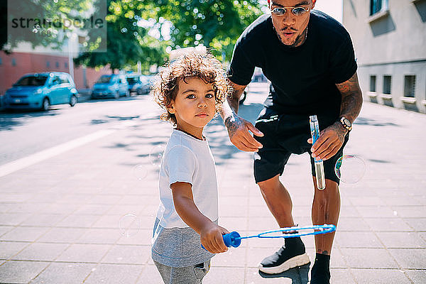 Vater und Sohn spielen mit Seifenblasen auf dem Bürgersteig