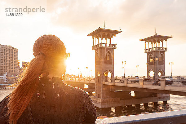 Weibliche Touristin mit roten Haaren  die bei Sonnenuntergang über die Stanley-Brücke schaut  Rückansicht  Alexandria  Ägypten