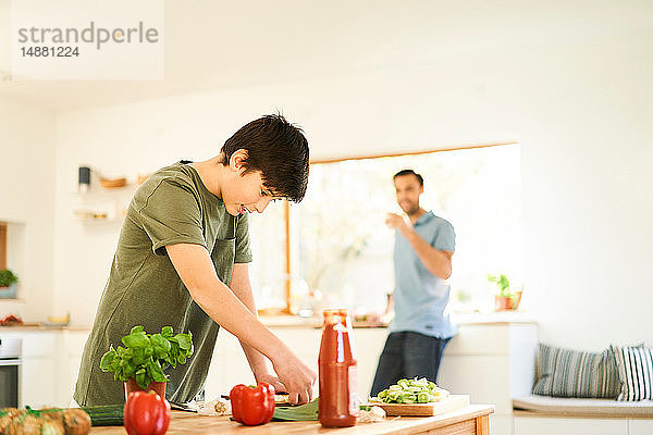 Junge bereitet Essen an der Küchentheke zu  Vater schaut zu