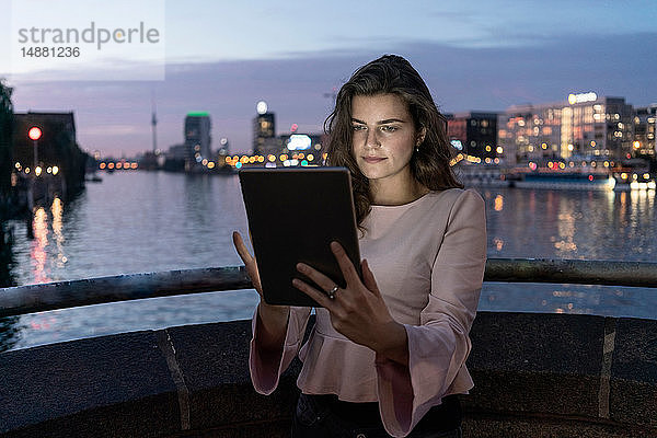 Junge Frau mit digitalem Tablett auf Brücke  Fluss und Stadt im Hintergrund  Berlin  Deutschland