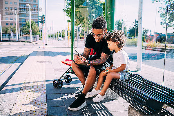 Vater unterrichtet Sohn mit Smartphone auf Bank