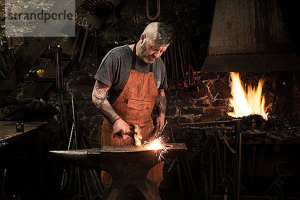 Ein reifer männlicher Schmied hämmert in der Werkstatt Metall auf den Amboss