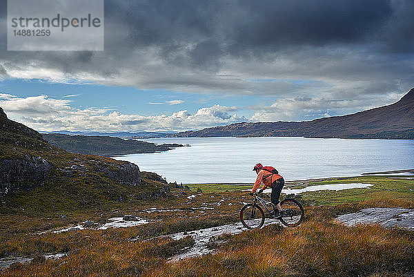 Männlicher Mountainbiker mit dem Fahrrad hinunter zum See in der Berglandschaft  Achnasheen  Schottische Highlands  Schottland