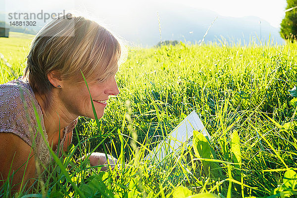 Frau liest Buch über Gras auf dem Land  Sonthofen  Bayern  Deutschland