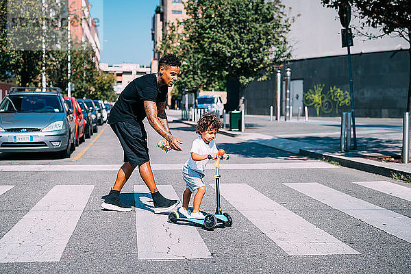 Vater hilft Sohn beim Schieben eines Rollers auf einem Fußgängerüberweg