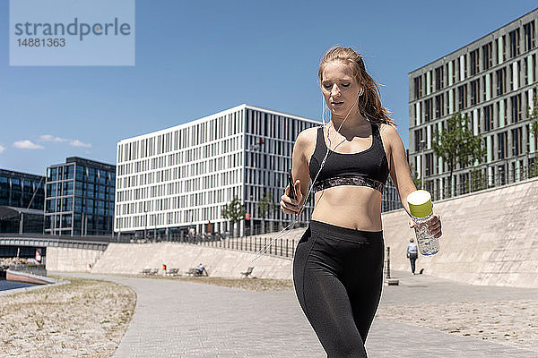 Junge Frau läuft und benutzt Smartphone in der Stadt  Berlin  Deutschland