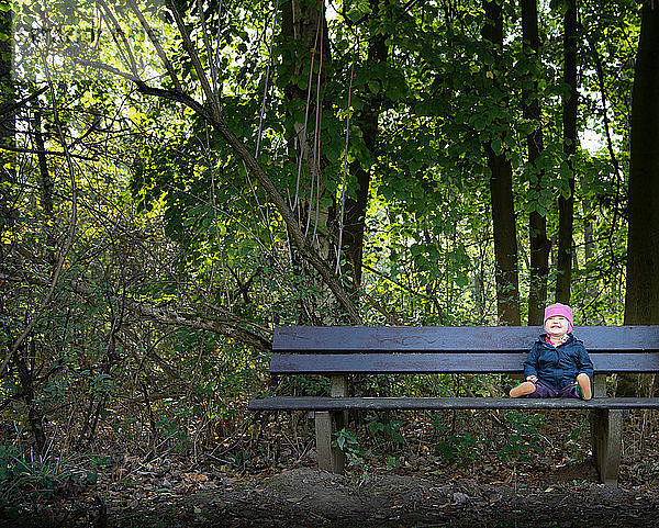 Lächelndes kleines Mädchen auf Parkbank am Wald