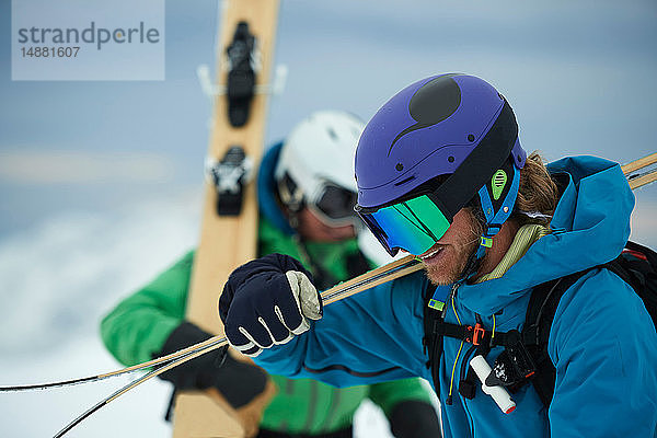 Zwei männliche Skifahrer tragen Skier im Schnee  Alpe-d'Huez  Rhône-Alpes  Frankreich