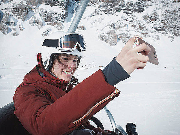 Junge Skifahrerin mit Helm und Skibrille  die mit Selfie auf Skilift fährt  Alpe Ciamporino  Piemont  Italien