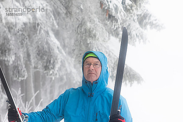 Älterer Mann mit Langlaufskiern in der Hand durch nebligen Wald  Porträt