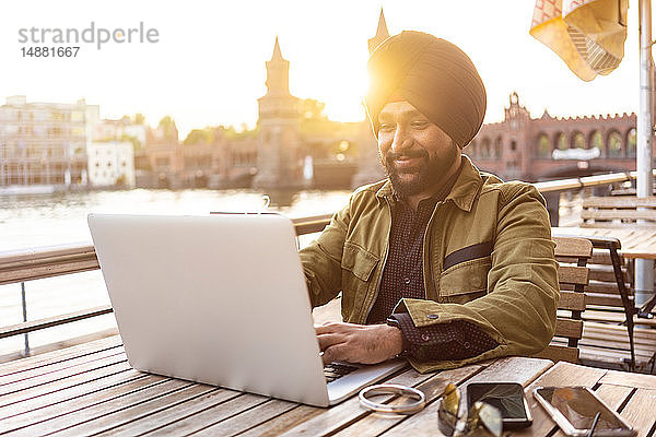 Indischer Mann mit Laptop im Café am Fluss  Berlin  Deutschland