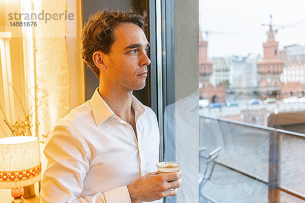 Mittlerer erwachsener Geschäftsmann  der während der Kaffeepause durch ein Bürofenster schaut