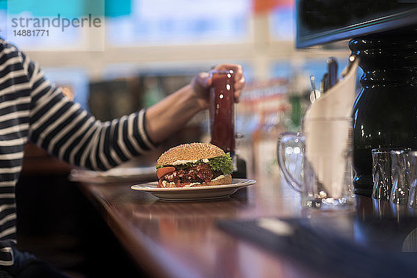 Frau mit Burgerteller auf der Theke eines Pubs