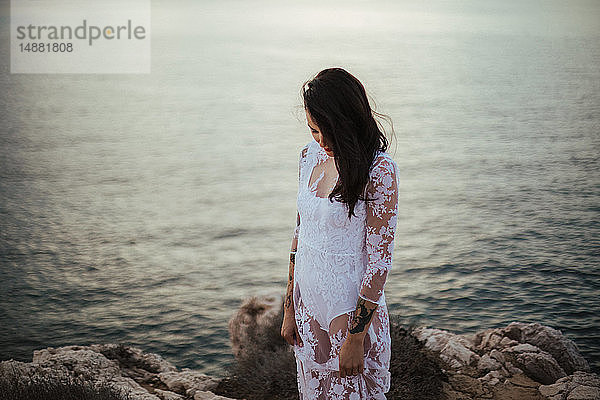 Glamouröse Frau in langem weißen Spitzenkleid auf Küstenfelsen  Porträt  Santa Teresa Gallura  Sardinien  Italien