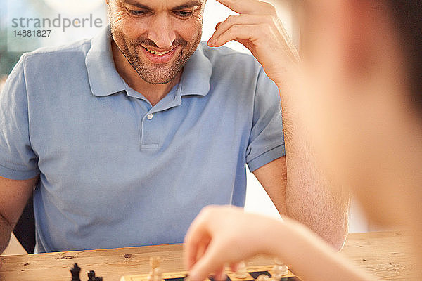 Junge und Vater spielen eine Schachpartie am Wohnzimmertisch  über der Schulter aus nächster Nähe