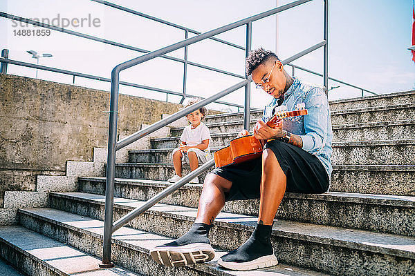 Kleinkind beobachtet Vater beim Gitarrespielen auf der Treppe