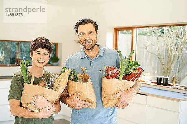 Junge und sein Vater in der Küche mit Einkaufstüten in der Hand  Porträt