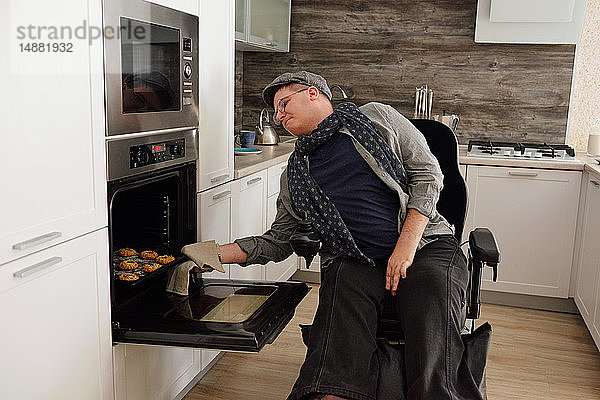 Körperlich behinderter Mann entfernt Tablett mit Keksen aus dem Ofen in der Küche