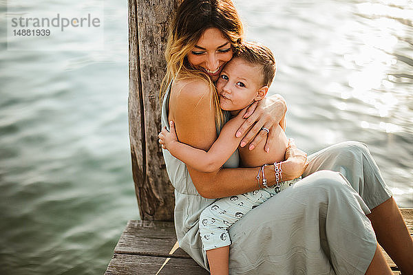 Mutter und Kleinkind Sohn sitzen umarmend am Pier  Porträt  Orta-See  Piemont  Italien