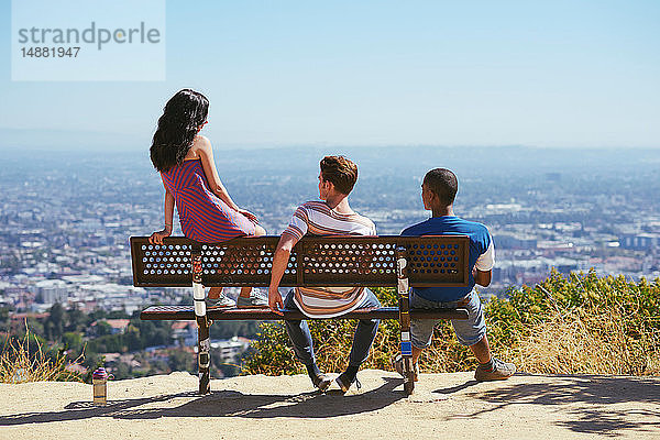 Drei junge erwachsene Freunde schauen von der Hügelbank aus auf das Stadtbild  Rückansicht  Los Angeles  Kalifornien  USA