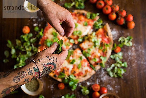 Chefkoch garniert Pizza mit Basilikumblättern auf der Küchenarbeitsplatte