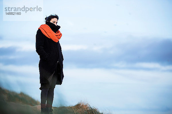 Frau schaut am Strand aufs Meer hinaus