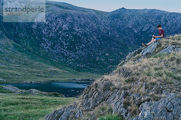 Junge liest Buch auf dem Gipfel eines Hügels  Snowdonia  Llanberis  Gwynedd  UK