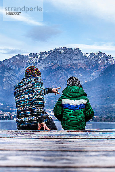Junge und Vater sitzen auf der Seebrücke  Rückansicht  Comer See  Onno  Lombardei  Italien