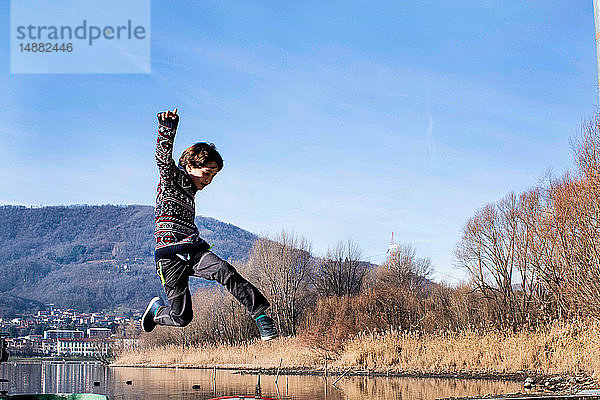 Junge springt mitten in der Luft am Seeufer  Comer See  Lecco  Lombardei  Italien