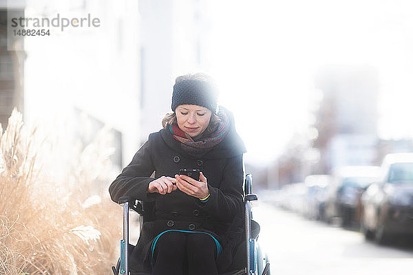 Frau im Rollstuhl mit Mobiltelefon auf der Strasse