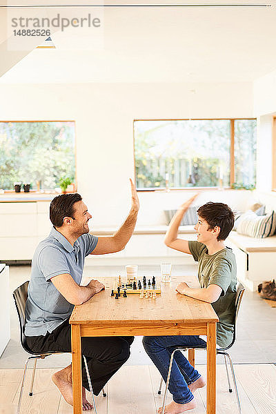 Junge und Vater spielen Schach am Wohnzimmertisch  High Fiving