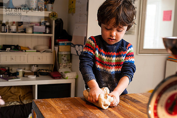 Kleinkind knet Teig auf Küchenarbeitsplatte