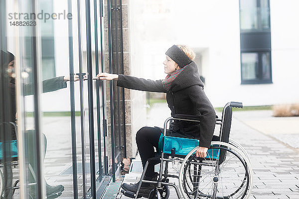 Frau im Rollstuhl öffnet Tür zum Gebäude