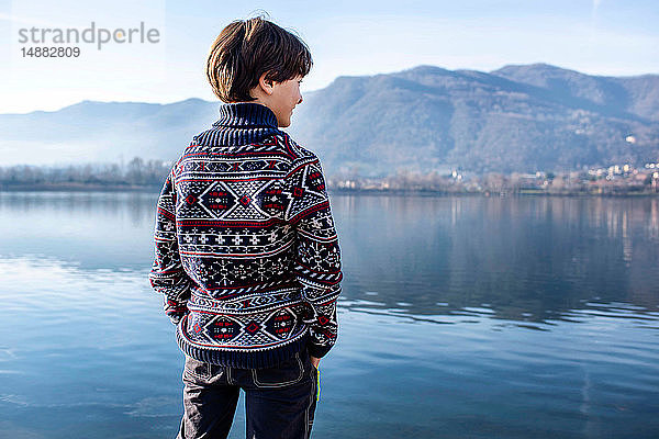 Junge schaut vom Seeufer aus  Rückansicht  Comer See  Lecco  Lombardei  Italien