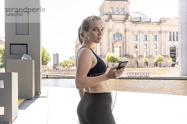 Junge Frau macht Pause vom Sport und benutzt Smartphone in der Stadt  Berlin  Deutschland